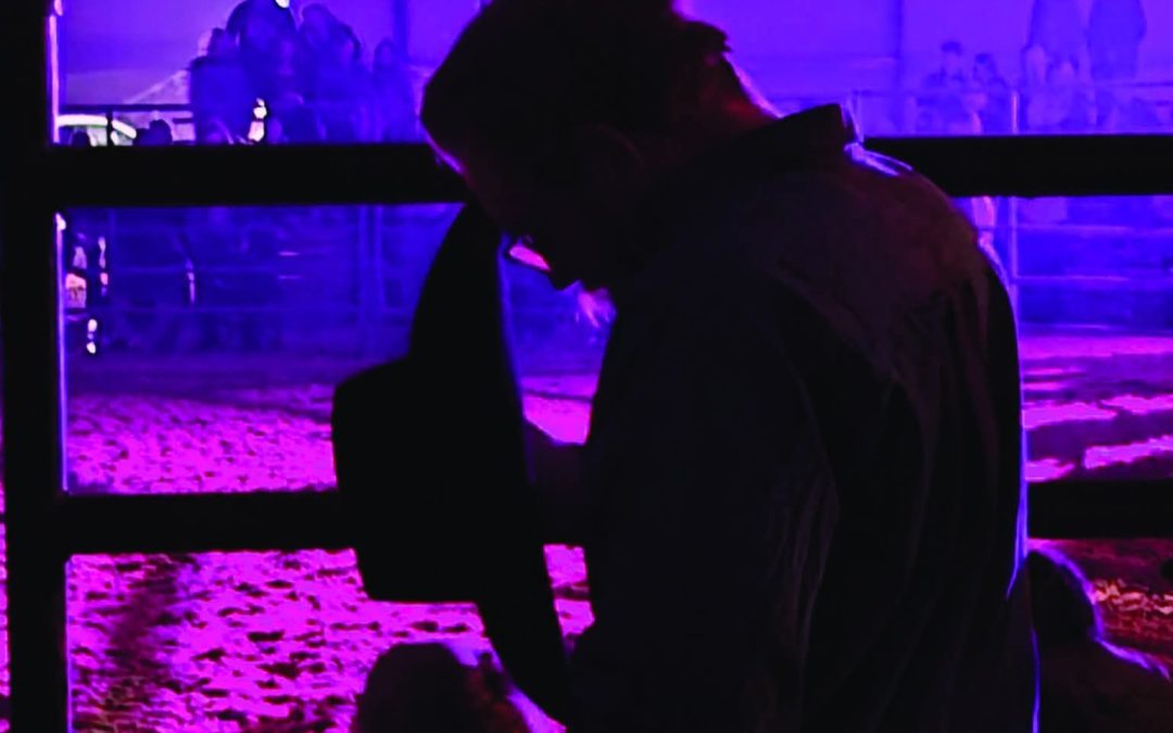 A Christian rodeo cowboy pauses to pray under the lights